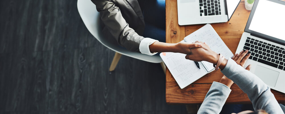 Two businesswomen shaking hands at table